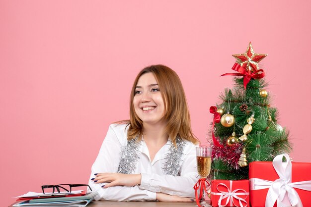 Vooraanzicht van vrouwelijke werknemer zittend rond kerstcadeautjes op roze