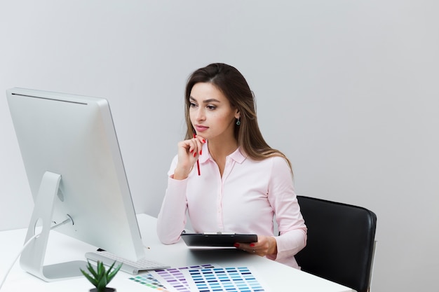 Vooraanzicht van werkende vrouw die computer bekijkt en tablet houdt