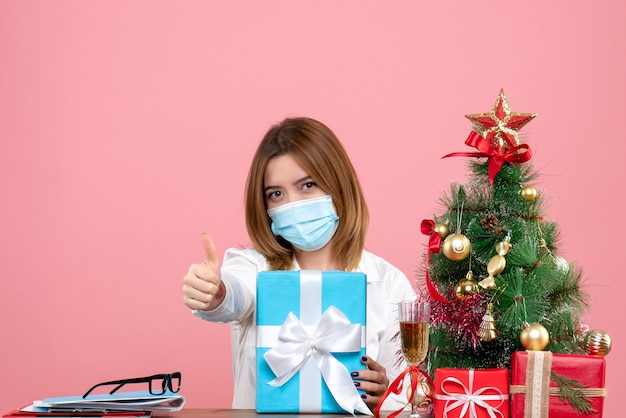 Vooraanzicht van werkneemster in steriel masker met cadeautjes op roze