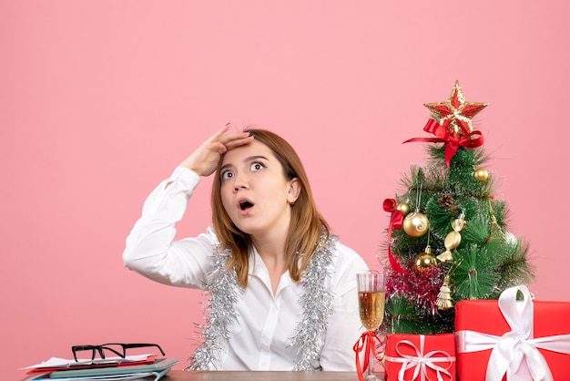 Vooraanzicht van werkneemster zittend achter haar tafel met kerstcadeautjes op roze