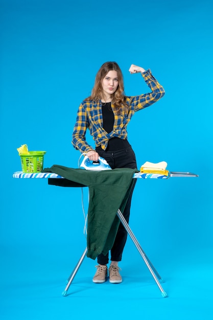 Vooraanzicht van zelfverzekerd mooi meisje dat de blouse aan boord in de wasruimte strijkt