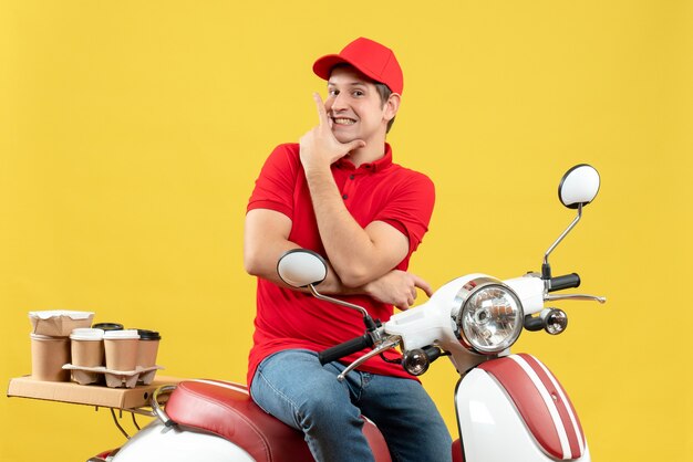 Vooraanzicht van zelfverzekerde gelukkige jonge kerel die rode blouse en hoed draagt die orden op gele achtergrond levert