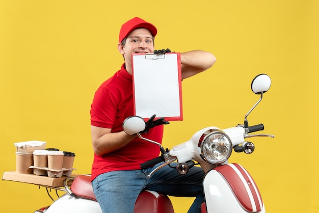 Vooraanzicht van zelfverzekerde koeriersmens die rode blouse en hoedshandschoenen in medisch masker draagt die ordezitting op het document van de autopedholding levert