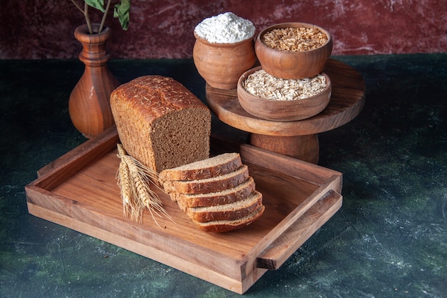 Vooraanzicht van zwarte sneetjes brood op bruin houten dienblad meel boekweit havermout op blauwe kleur verontruste achtergrond