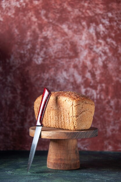 Vooraanzicht van zwarte sneetjes brood op een houten bord en mes op gemengde kleuren noodlijdende achtergrond