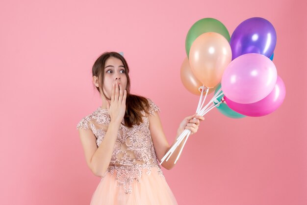 Vooraanzicht verbaasd feestmeisje met feestmuts met ballonnen op zoek naar iets