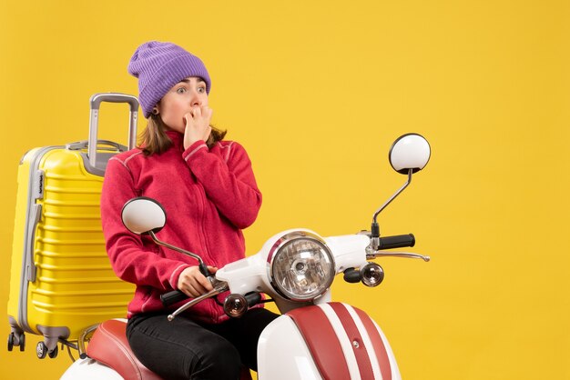 Vooraanzicht verbaasde jonge vrouw op bromfiets met gele koffer