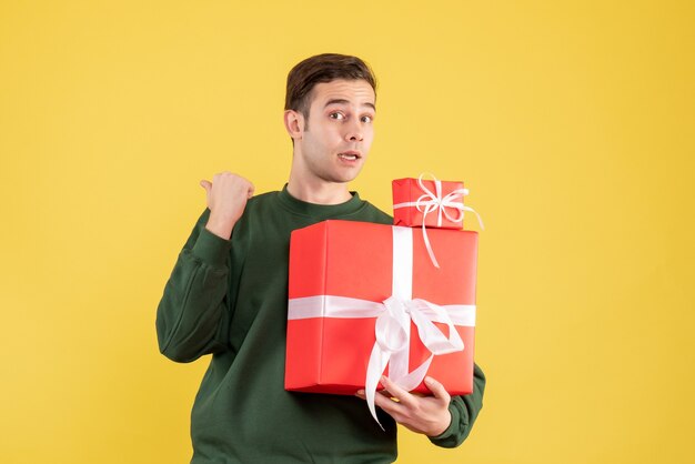 Vooraanzicht verrast jonge man met kerst cadeau staande op geel