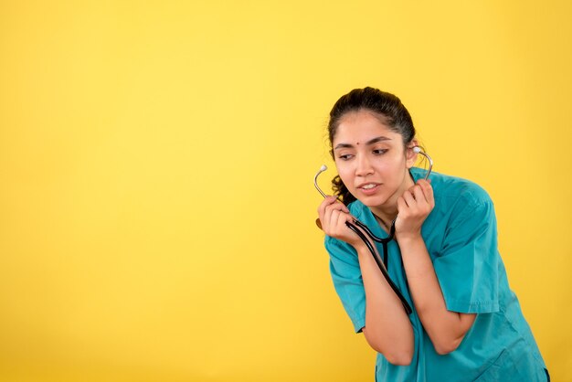 Vooraanzicht verrast vrouw arts in uniforme holdingsstethoscoop op gele achtergrond