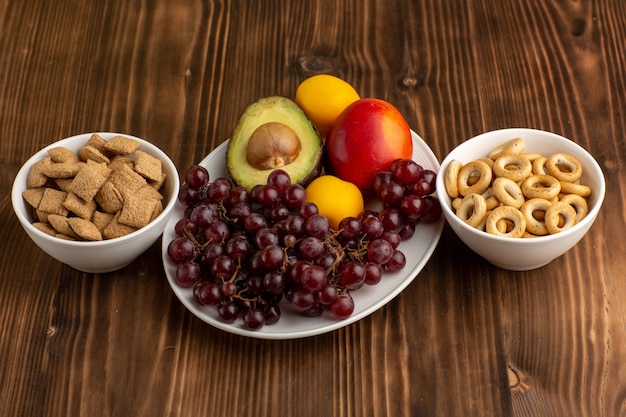 Vooraanzicht vers fruit druiven mango avocado en grapefruit met crackers op bruin bureau