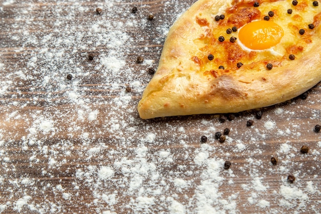 Vooraanzicht vers gebakken brood met gekookt ei en bloem op bruin bureaudeeg bak het broodje van het eierbrood