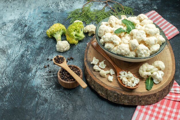 Vooraanzicht verse bloemkool met lepels en peper op lichtgrijze ondergrond