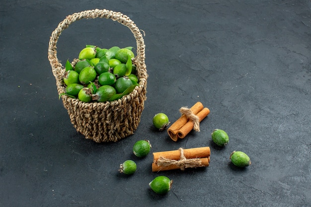 Gratis foto vooraanzicht verse feijoas in mand kaneelstokjes op donkere ondergrond