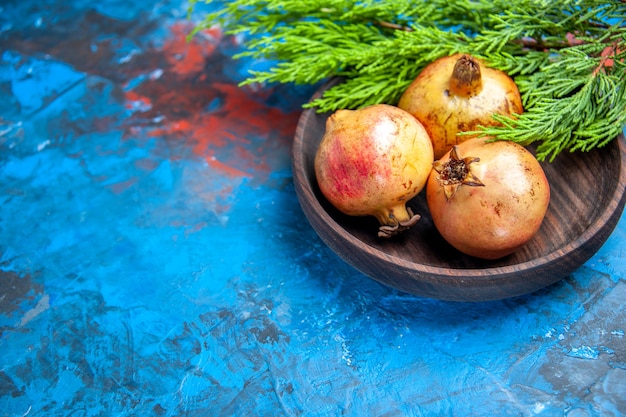 Vooraanzicht verse granaatappels in houten kom dennenboomtak op blauw