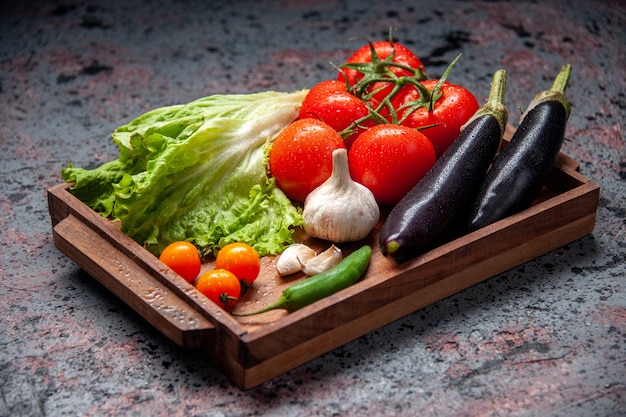 vooraanzicht verse groenten rode tomaten knoflook groene salade en aubergines in houten bord op blauwe achtergrond