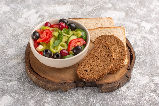 Vooraanzicht verse groentesalade met gesneden komkommers, tomaten, olijven en witte kaas binnen plaat met brood op de grijze maaltijd van de de salade van het bureau plantaardige voedsel