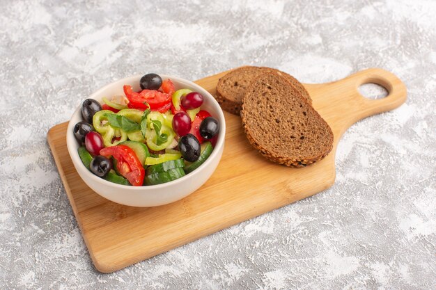 Vooraanzicht verse groentesalade met gesneden komkommers, tomaten, olijven en witte kaas in plaat met broodbroodjes op het grijze bureau