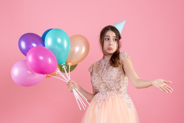 Vooraanzicht verward meisje met feestdop openen haar hand met ballonnen