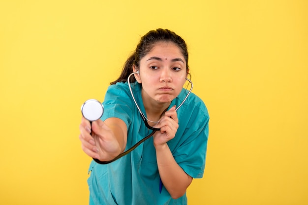 Vooraanzicht verwarde vrouw arts in uniform met behulp van stethoscoop op gele achtergrond
