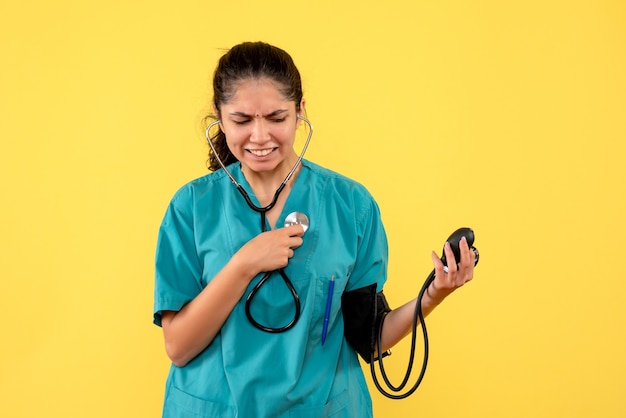 Vooraanzicht verwarde vrouwelijke arts in uniforme bedrijf bloeddrukmeters staande op gele achtergrond