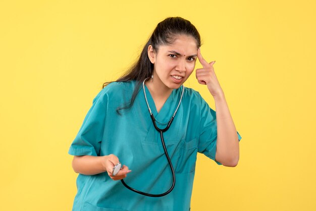 Vooraanzicht vrij vrouwelijke arts met stethoscoop in haar hand vinger naar haar tempel op gele achtergrond
