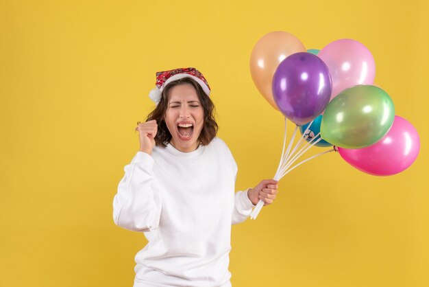 Vooraanzicht vrij wijfje dat kleurrijke ballons op geel houdt