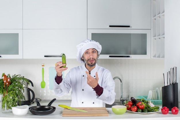 Vooraanzicht vroeg zich af mannelijke chef-kok in uniform die komkommer in de keuken vasthoudt