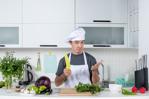 Vooraanzicht vroeg zich af mannelijke chef-kok in uniform met mes in de keuken