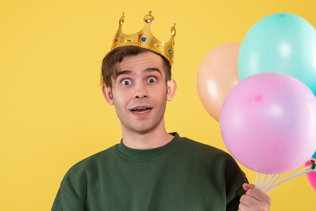 Vooraanzicht vroeg zich jonge man af met kroon die ballonnen op geel hield