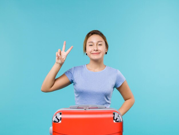 Vooraanzicht vrouw in vakantie met haar rode tas lachend op de blauwe achtergrond vakantie vliegtuig reis reis zeereis
