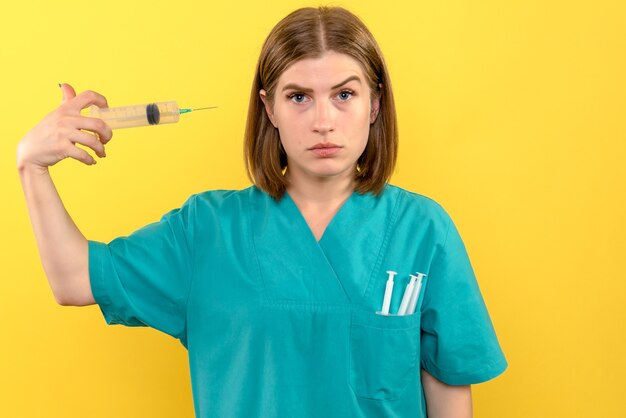 Vooraanzicht vrouwelijke arts die grote injectie op gele ruimte houdt