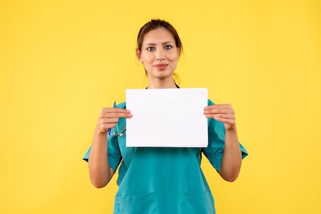 Vooraanzicht vrouwelijke arts die in medisch overhemd document analyse op gele achtergrond houdt
