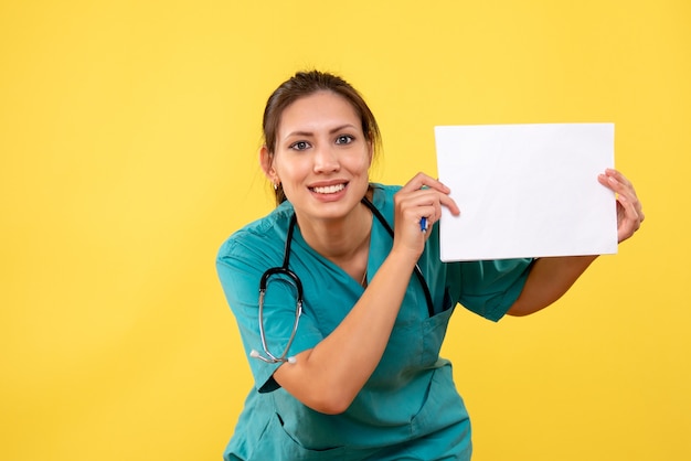 Vooraanzicht vrouwelijke arts die in medisch overhemd document analyse op gele achtergrond houdt