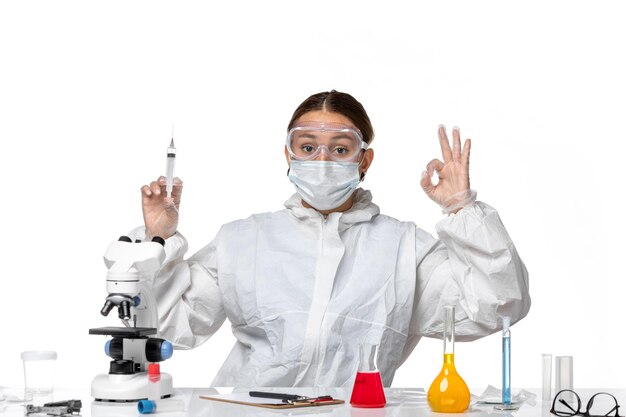 Vooraanzicht vrouwelijke arts in beschermend pak en met injectie van de maskerholding op lichte witte achtergrond de covid pandemie van de virusgeneeskunde