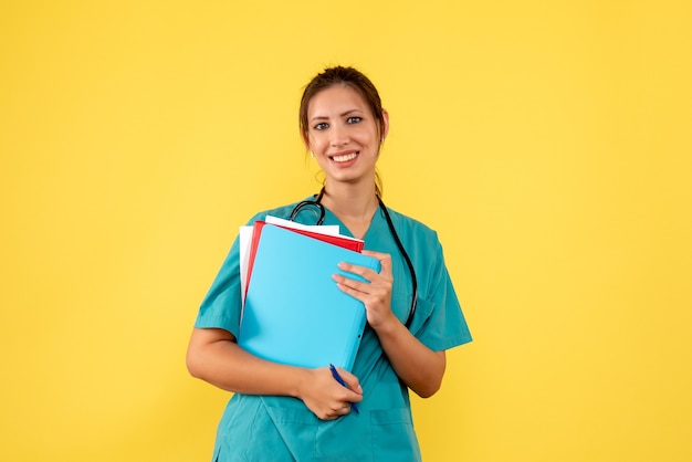Vooraanzicht vrouwelijke arts in de analyse van de medische overhemdsholding op gele achtergrond