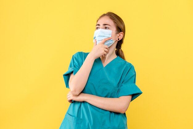 Vooraanzicht vrouwelijke arts in masker die op geel pandemisch covidgezondheidsvirus als achtergrond denken