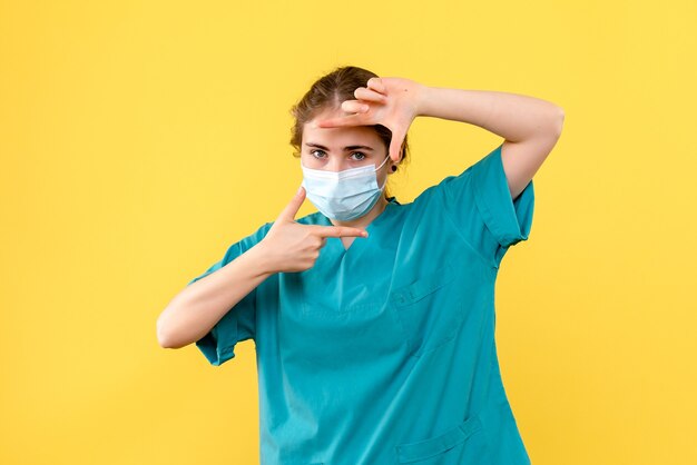 Vooraanzicht vrouwelijke arts in masker op gele achtergrond gezondheid ziekenhuis pandemie covid