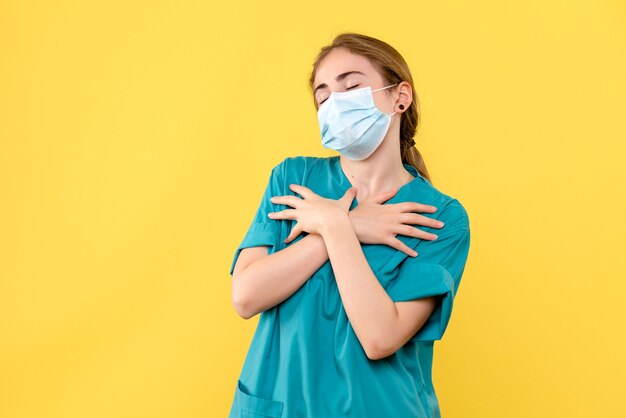 Vooraanzicht vrouwelijke arts in masker op het gele bureau de gezondheid van het ziekenhuis covid-pandemie