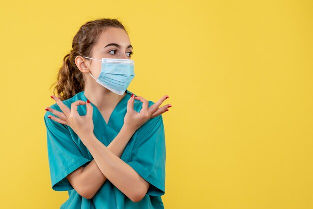 Vooraanzicht vrouwelijke arts in medisch overhemd en masker, gezondheid pandemie covid-19 virus uniforme kleur