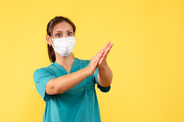 Vooraanzicht vrouwelijke arts in medisch overhemd en masker op gele achtergrond