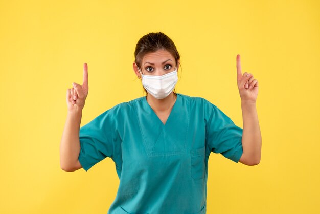 Vooraanzicht vrouwelijke arts in medisch overhemd en masker op gele achtergrond