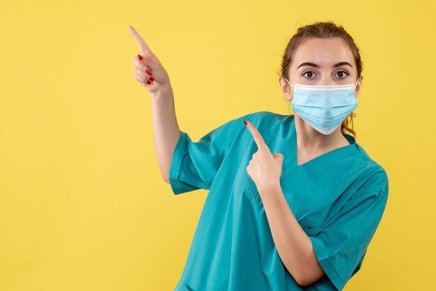 Vooraanzicht vrouwelijke arts in medisch overhemd en masker, pandemie covid-19 virus uniforme kleur