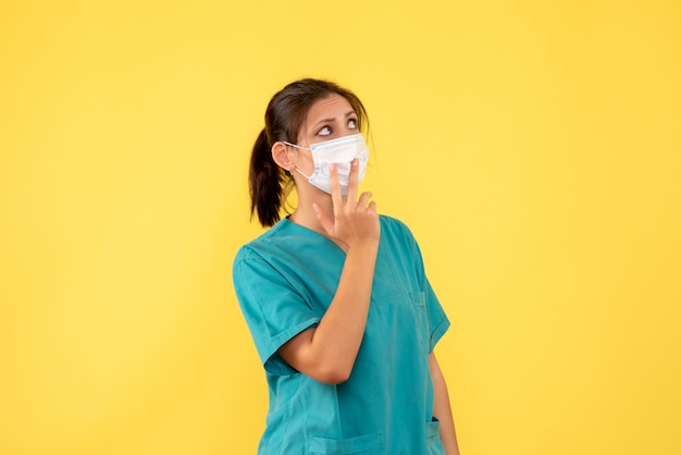 Vooraanzicht vrouwelijke arts in medisch overhemd en met steriel masker op gele achtergrond