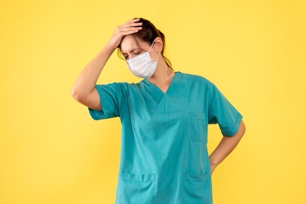 Vooraanzicht vrouwelijke arts in medisch overhemd en met steriel masker op gele achtergrond
