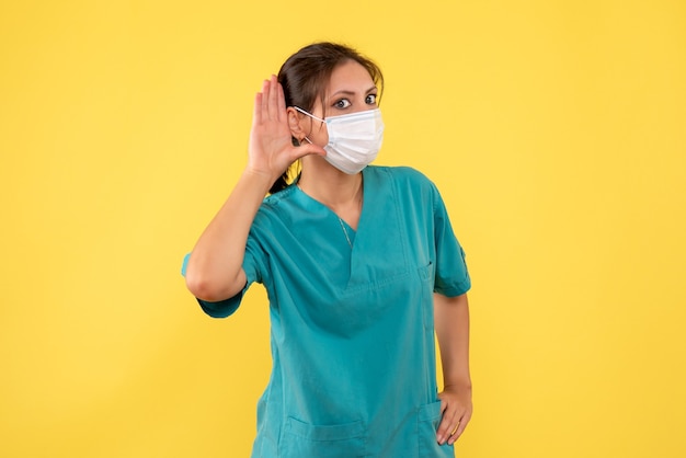 Vooraanzicht vrouwelijke arts in medisch overhemd en steriel masker op gele achtergrond