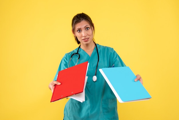 Vooraanzicht vrouwelijke arts in medisch overhemd met notities op gele achtergrond