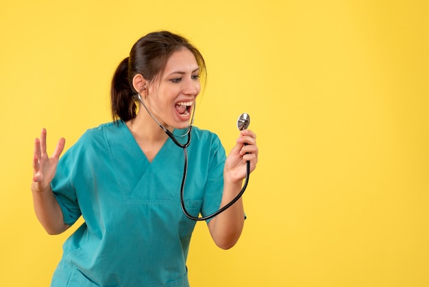 Vooraanzicht vrouwelijke arts in medisch overhemd met stethoscoop op gele achtergrond