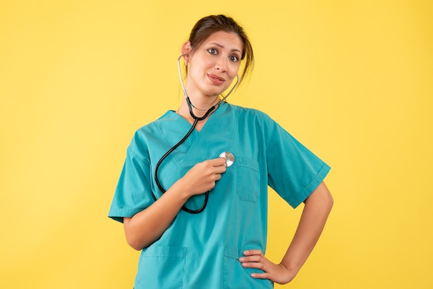 Gratis foto vooraanzicht vrouwelijke arts in medisch overhemd op gele achtergrond