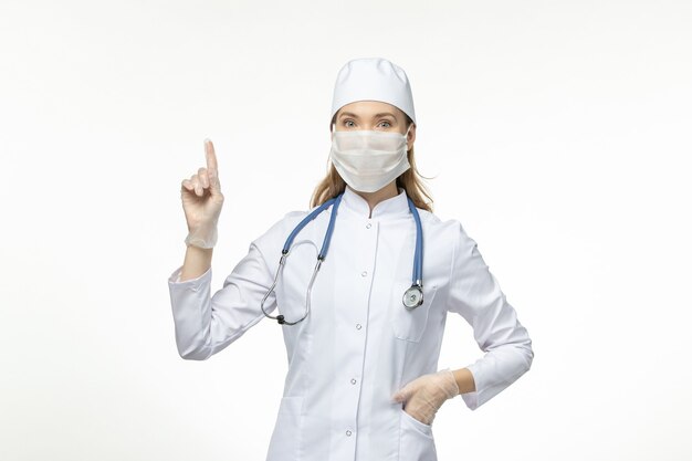 Vooraanzicht vrouwelijke arts in medisch pak draagt masker vanwege coronavirus op lichtwitte vloerziekte covid- pandemische virusziekte