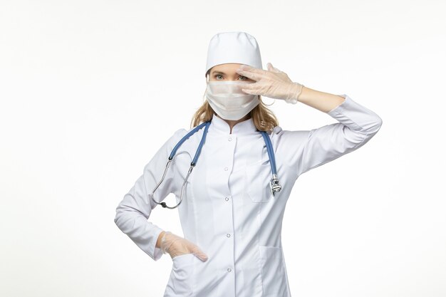 Vooraanzicht vrouwelijke arts in medisch pak masker en handschoenen dragen vanwege coronavirus op wit bureau ziekte covid- pandemische ziekte ziekte